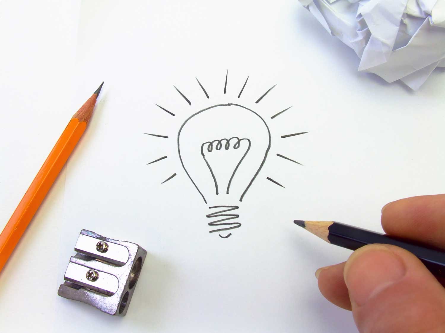 hand drawing a light bulb with a pencil with another pencil sharpener and ball of crumpled paper