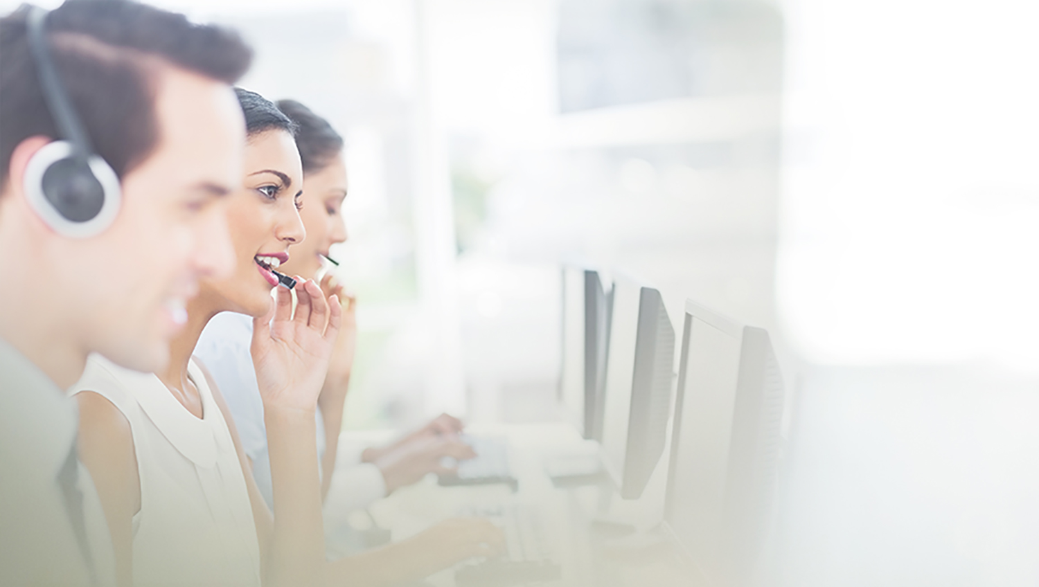 three customer service agents wearing headsets at computers in an all white blown out room