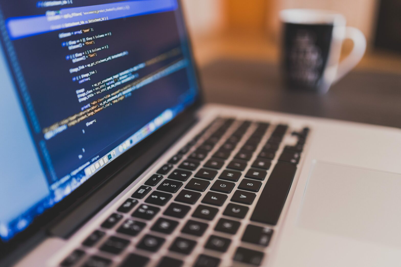 laptop with code on screen and blurry coffee cup in the background