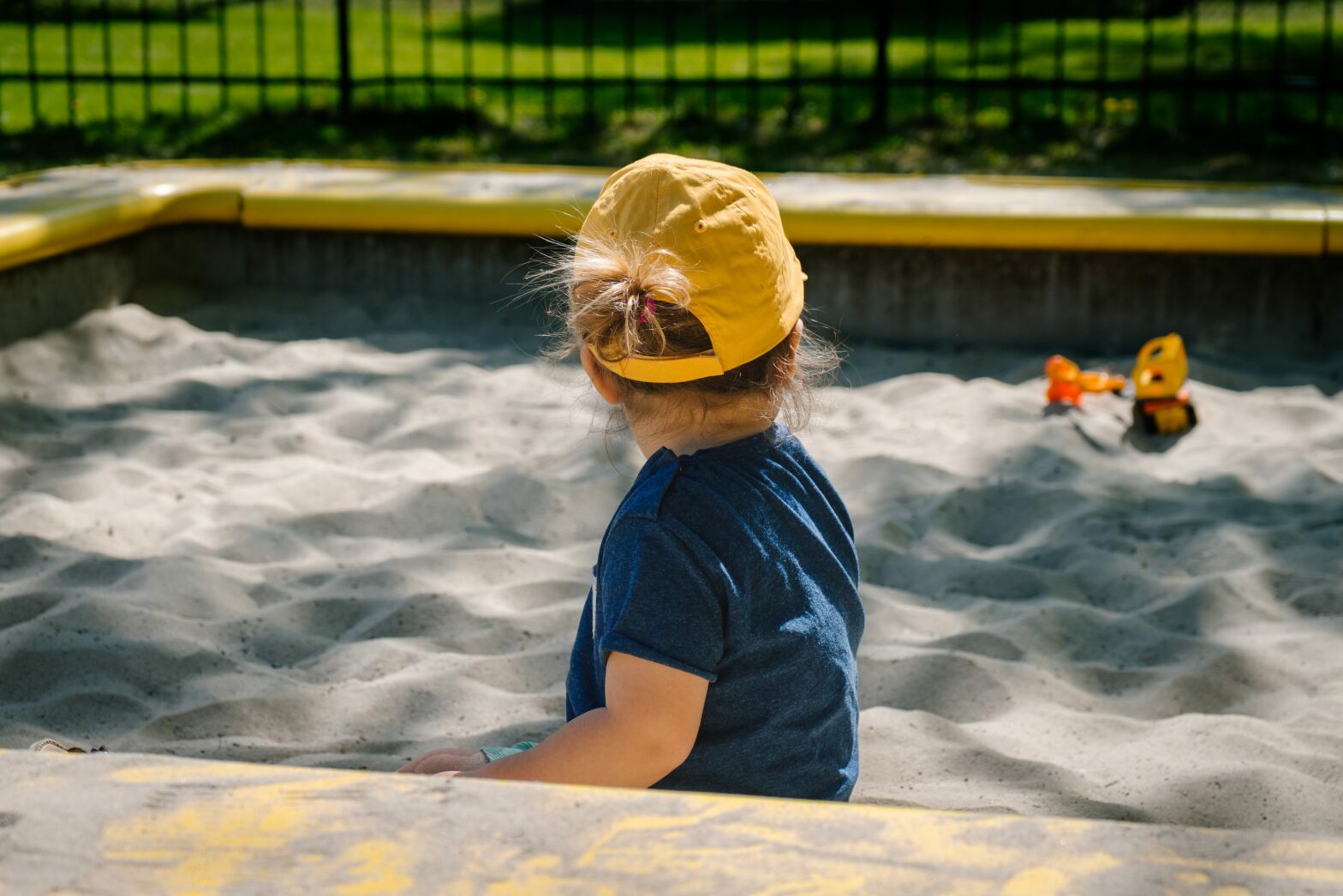 child in yellow hat and blue shirt in a sandbox