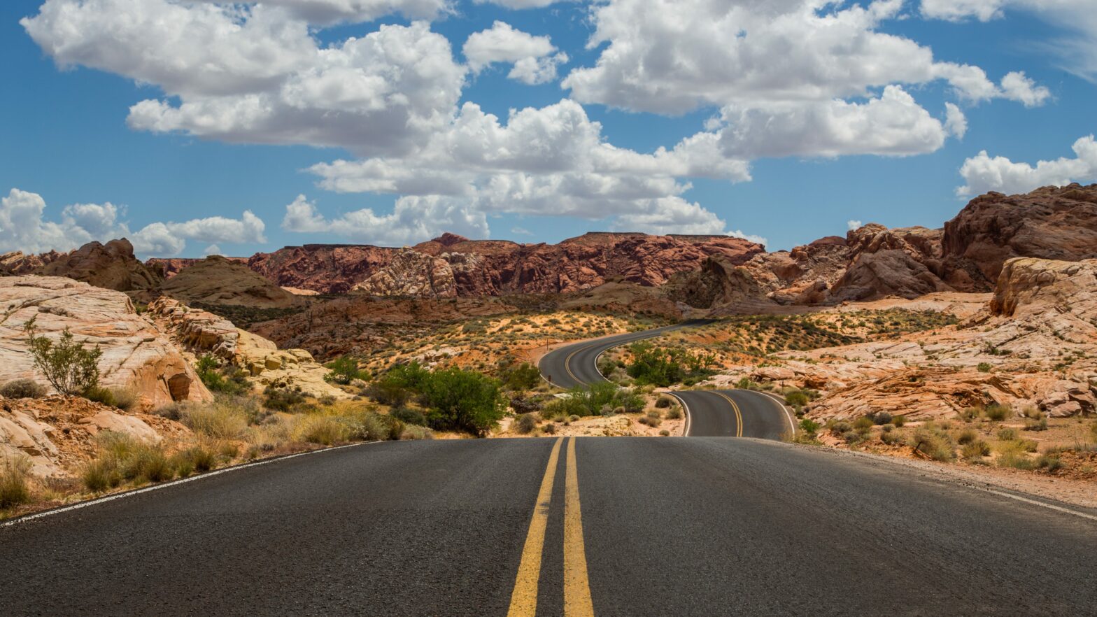 winding road running through a desert with blue skies and clouds