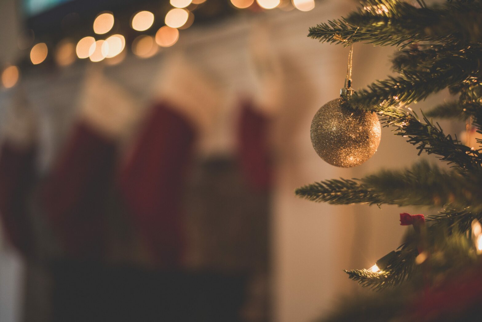 close up of ornament on christmas tree with blurry stockings and lights in the background