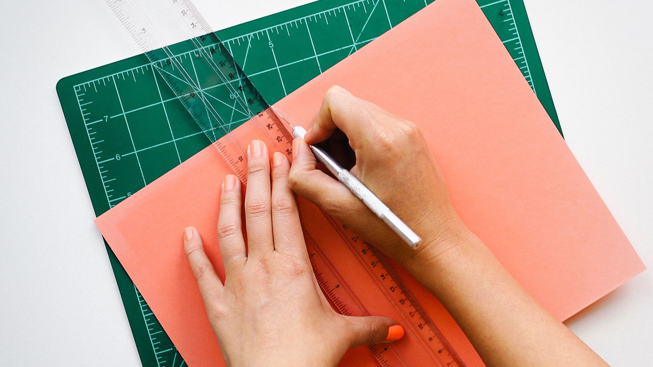 Hands cutting paper with knife and ruler